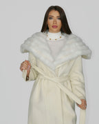 Woman wearing a white fur shawl over a cream coat, standing front-facing