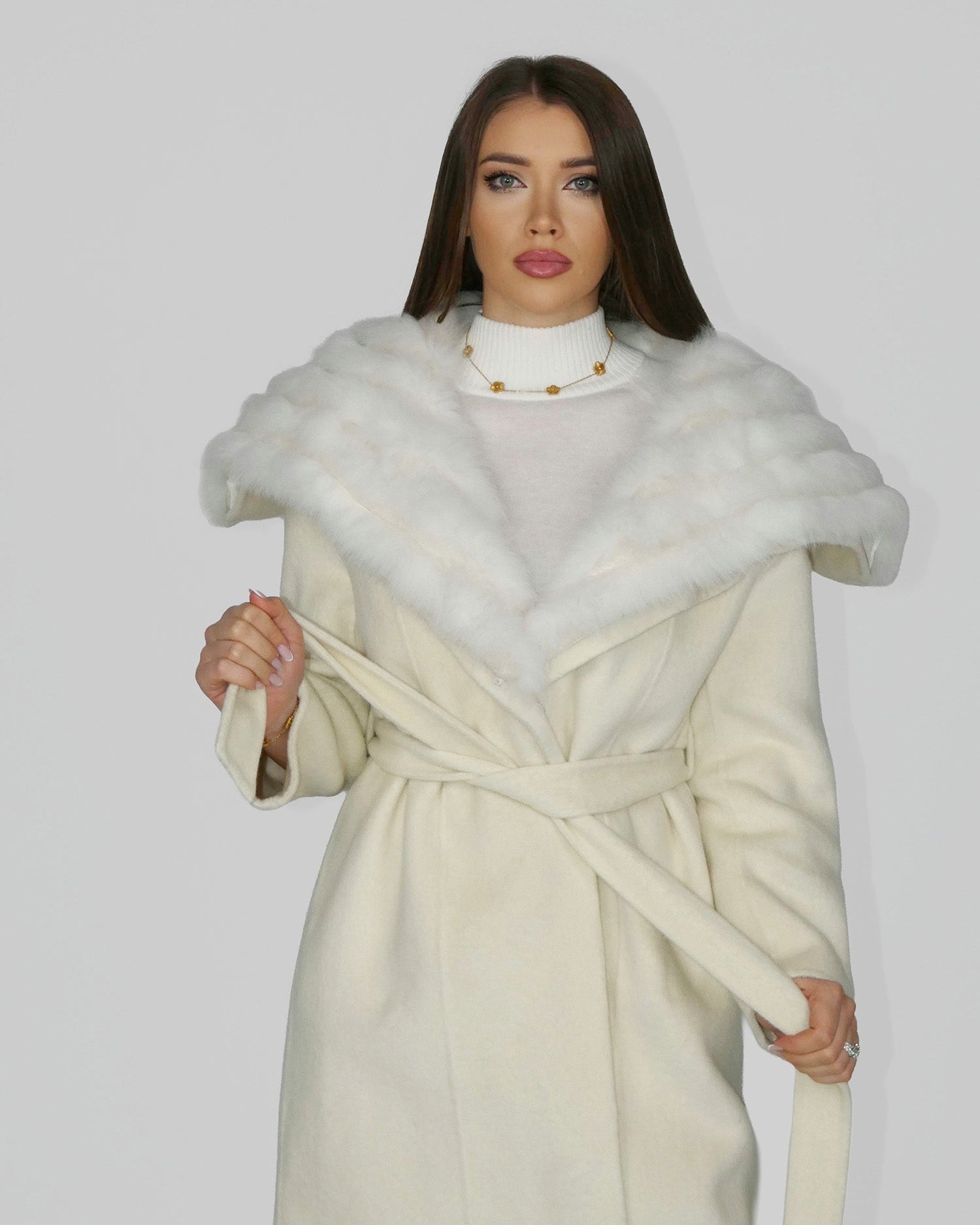Woman wearing a white fur shawl over a cream coat, standing front-facing