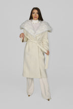 Woman wrapped in a large white fur shawl over a long cream coat