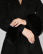 Close-up of hands adjusting the sleeve of a black coat with fur cuffs