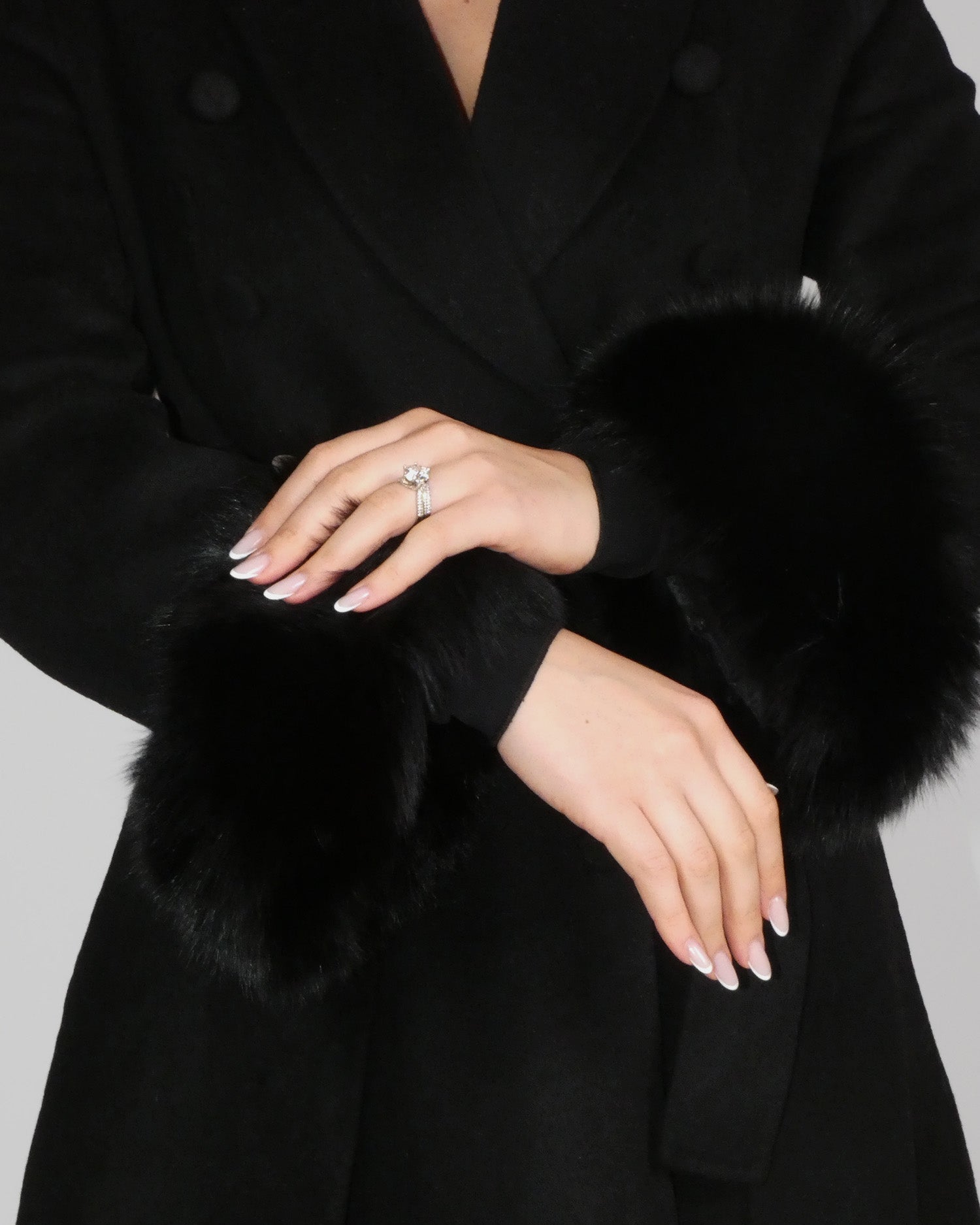 Close-up of hands adjusting the sleeve of a black coat with fur cuffs