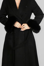 Woman wearing a long black coat, holding the front lapels