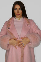 Woman wearing a pink fur coat with belt, holding the front