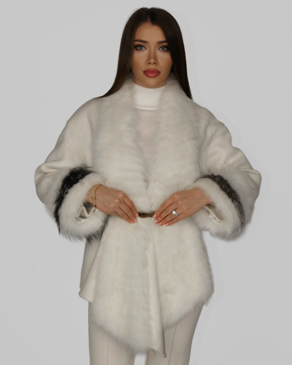 Woman wearing a white textured fur coat, facing forward with hands at waist