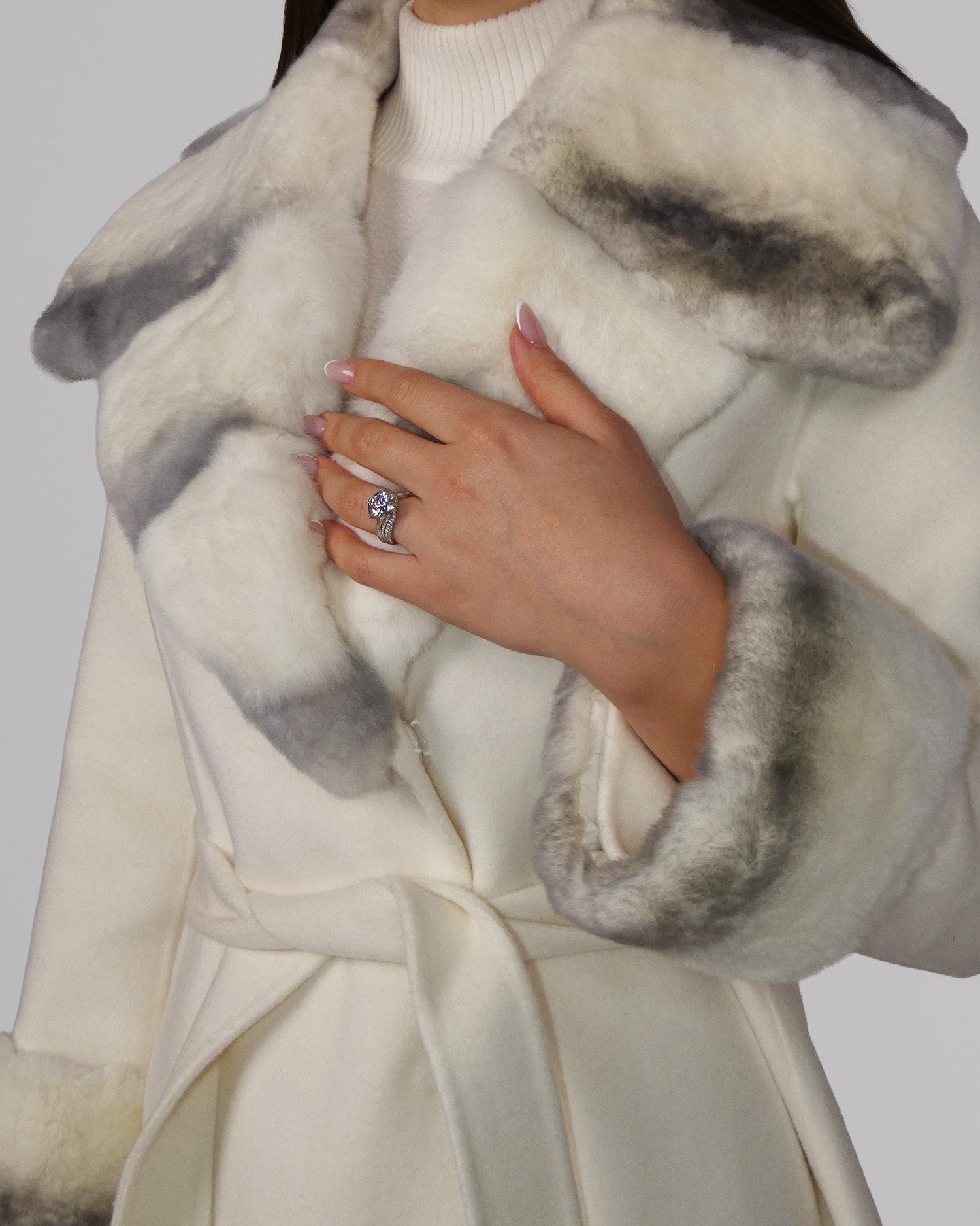 Close-up of hands holding a white fur coat with grey trim