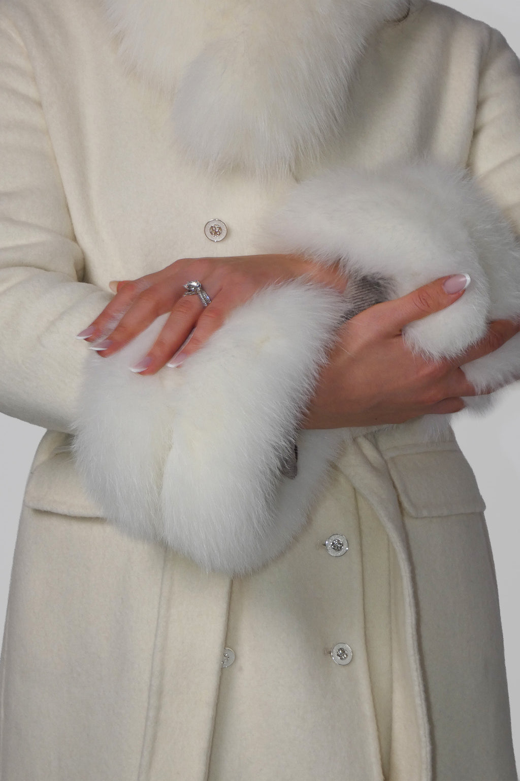 Close-up of hands adjusting the belt of a beige fur-trimmed coat